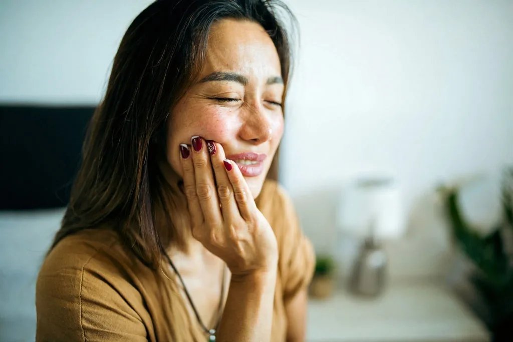 Woman wincing from tooth sensitivity while drinking a cold drink